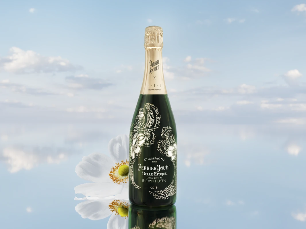 Perrier-Jouët Belle Epoque 2018 Limited Cuvée by Iris van Herpen, bottle with golden floral artwork beside a white Japanese anemone against a reflected sky
